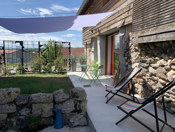 Un patio con un muro de piedra, un regador azul y una mesa con sillas.