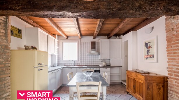 Una cocina con armarios blancos, techo de madera y piso de baldosas.