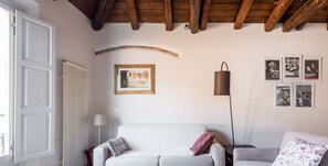 A modern living room with a white sofa, a grey sofa, and a patterned throw pillow. There is a framed picture on the wall and a lamp beside the grey sofa.