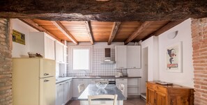 Una cocina con armarios blancos, techo de madera y piso de baldosas.