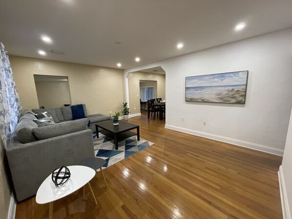 A modern living room with hardwood flooring, a grey sofa, a coffee table, and a dining area with chairs.