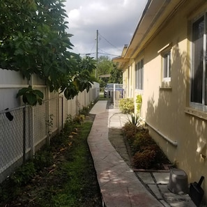 A narrow pathway flanked by a chain-link fence and a building with a yellow exterior.