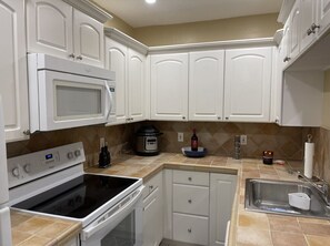 A kitchen with white cabinets, a stove, an oven, a microwave, a sink, and a slow cooker.