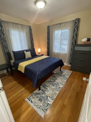 A bedroom with a bed, a bedside lamp, a dresser, and a patterned rug.