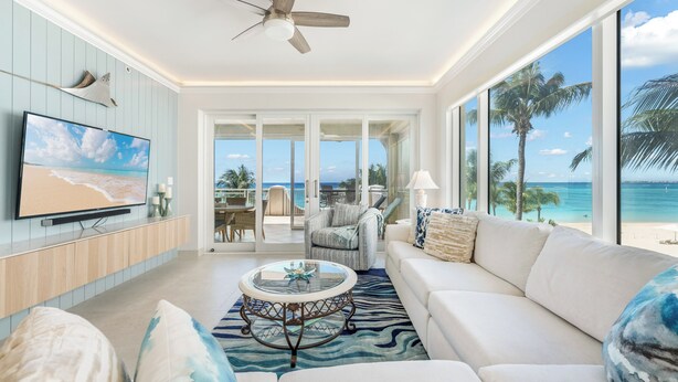 Un salon spacieux doté d’une grande télévision, de sièges confortables, d’un ventilateur de plafond et offrant une vue sur la plage grâce à de grandes fenêtres.
