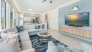 Un salon moderne avec un canapé d’angle, une table basse en verre et un téléviseur à écran plat fixé au mur.