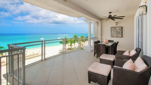 A balcony with a view of the beach and ocean, furnished with wicker chairs and a table. - Beachcomber 19 by Grand Cayman Villas (7 Mile Beach)
