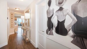 A hallway with a mirrored wall featuring a black and white photograph of a woman in a dress. There is a console table with decorative items and a vase. - Beachcomber 19 by Grand Cayman Villas (7 Mile Beach)
