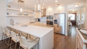 A modern kitchen with a central island, stainless steel appliances, and pendant lighting. - Beachcomber 19 by Grand Cayman Villas (7 Mile Beach)