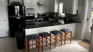 A modern kitchen with white cabinets, a black refrigerator, a microwave, and a sink. There are four wooden stools with patterned cushions. - Azalea Cottage 1Br/1Ba with spacious Deck overlooking LKN and 2 Private docks.   (Mooresville)