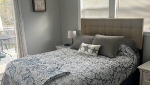 A bedroom with a large bed, a nightstand, a ceiling fan, and a window with blinds. - Azalea Cottage 1Br/1Ba with spacious Deck overlooking LKN and 2 Private docks.   (Mooresville)