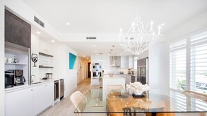 A modern kitchen with white cabinets, a glass dining table, wicker chairs, and a chandelier.