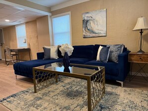 A living room with a blue sofa, a glass coffee table, and a painting on the wall. - Spacious Home with Pet-Friendly Yard (Charlotte)