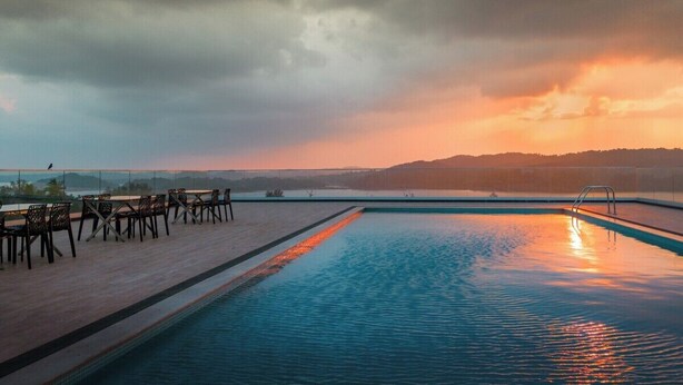 Piscina com vista para o pôr do sol e colinas ao longe.