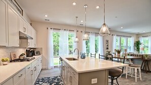 Una cocina moderna con una isla central, iluminación colgante y vistas al exterior gracias a amplios ventanales.