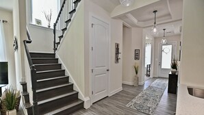 Un interior moderno con una escalera de madera oscura, una puerta blanca y un pasillo que conduce a un comedor.