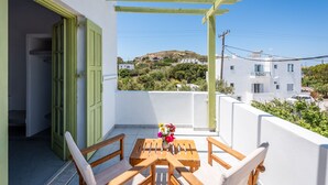 Un balcon avec une table et des chaises en bois, une porte verte et une vue sur une colline parsemée de bâtiments.