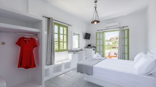 Une chambre d’hôtel avec un lit, une télévision, une fenêtre donnant sur un beau paysage et une robe rouge suspendue à un portant.