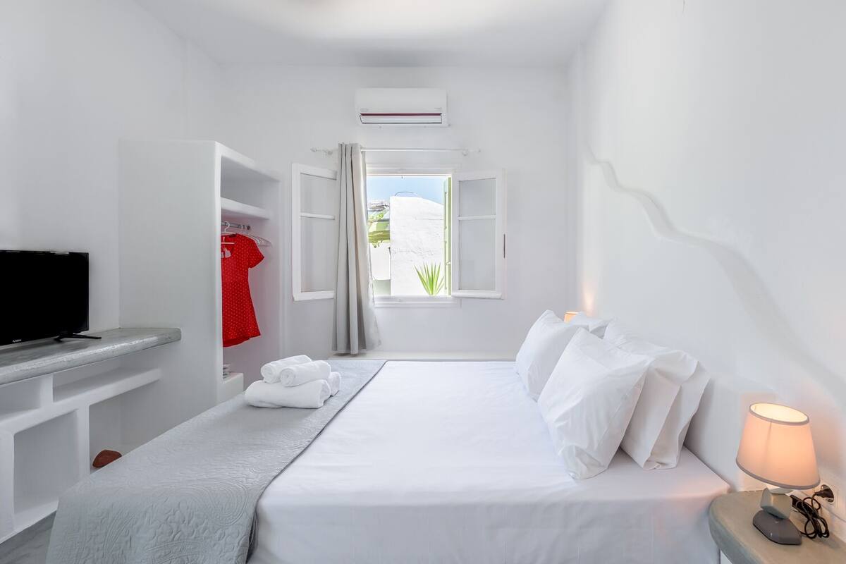 A hotel room with a bed, a TV, a desk, and a window with curtains.
