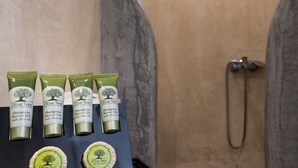 Quatre tubes de shampoing et de gel douche à l’huile d’olive, ainsi que deux savons à l’huile d’olive, sont présentés sur une étagère dans une salle de bain équipée d’une douche.