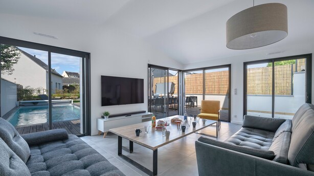 A modern living room with a pool view, a flat-screen TV, and a dining area. - Modern house with pool for 15 - Center town (Saint-Gildas-de-Rhuys)