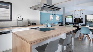 A modern kitchen with a central island, bar stools, and a dining area with a TV. - Modern house with pool for 15 - Center town (Saint-Gildas-de-Rhuys)