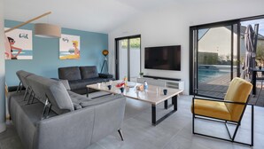 A modern living room with a grey sofa, a yellow armchair, a wooden coffee table, and a TV. - Modern house with pool for 15 - Center town (Saint-Gildas-de-Rhuys)