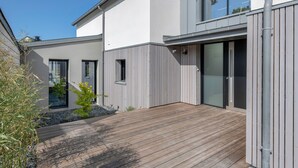 A modern house with a wooden deck, a small garden, and a large sliding glass door. - Modern house with pool for 15 - Center town (Saint-Gildas-de-Rhuys)