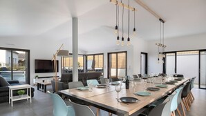 A modern dining area with a long table set for a meal, surrounded by chairs, and a TV mounted on the wall. - Modern house with pool for 15 - Center town (Saint-Gildas-de-Rhuys)