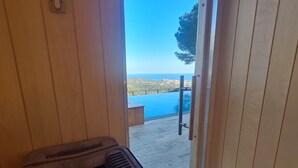 Un cuarto de sauna con una puerta de madera que da a un balcón con vista al mar.