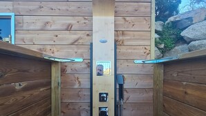 Una sauna de madera con un cabezal de ducha central, un panel de control y una manguera.