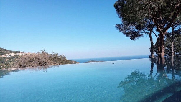 Una piscina infinita con agua azul cristalina, rodeada de árboles y con vistas a una costa lejana.