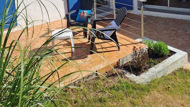Ein weißes Gebäude mit blauen Fensterläden, einem Ziegeldach und einer Terrasse mit Stühlen und einem Tisch.