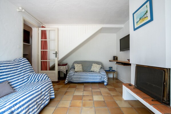 A living room with a sofa, a small table, a television, and a fireplace. - Large house for 6 people - 300m from the beach (Barbâtre)