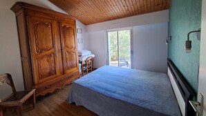 Ein Schlafzimmer mit Holzschrank, Bett und Stuhl, sowie eine Glastür zum Balkon.