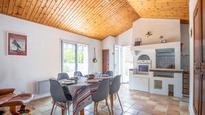 Ein Essbereich mit Holzbalkendecke, einem Tisch mit Stühlen und einer Küchenzeile mit Einbauofen und Spüle.
