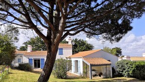 Ein traditionelles Haus mit Ziegeldach, ein großer Baum im Vordergrund und ein gepflegter Rasen.