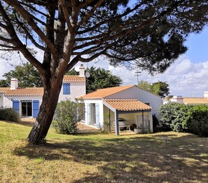 Une maison traditionnelle avec un toit en tuiles, un grand arbre au premier plan et une pelouse bien entretenue.