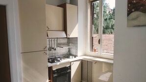 Una cocina compacta con estufa a gas, horno y lavamanos, una ventana con vista a un tejado de baldosas y un pequeño estante sobre el lavamanos.