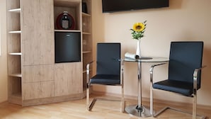 Quarto moderno com armário embutido de madeira, televisão de tela plana, duas cadeiras pretas, mesa redonda pequena e um vaso com um girassol.