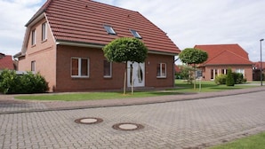 Uma casa de dois andares de tijolo com telhado vermelho, um pequeno jardim frontal e um caminho de entrada pavimentado.