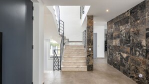 Un interior moderno con una escalera, una pared oscura con textura similar a la piedra y un suelo de color claro.