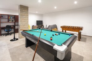 Ein Billardtisch mit Kugeln, ein Fernseher, ein Bücherregal und ein Schreibtisch in einem Zimmer.