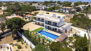 Una casa moderna de dos pisos con un panel solar en la azotea, una piscina y un jardín bien cuidado.