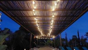 Una terraza de madera al aire libre con techo de paja, luces colgantes y sillones de descanso.