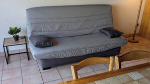 Ein graues Sofa mit zwei Kissen, ein kleiner Holztisch mit einem Blumentopf und eine Stehlampe.