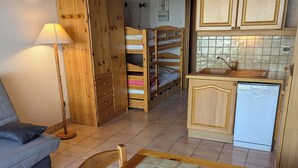Ein kleines Zimmer mit Etagenbett, einer Schlafcouch, einem Esstisch und einer Küchenzeile.