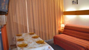 Hotellihuoneessa on ruokapöytä, jonka päällä on lautasia ja laseja, sohva, televisio ja lamppu.