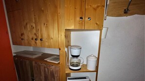 Kompakti keittiö, jossa on puukaapit, kahvinkeitin, leivänpaahdin ja pieni pesuallas.