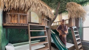 Bunk beds with a slide, a ladder, and a tree mural in a room.